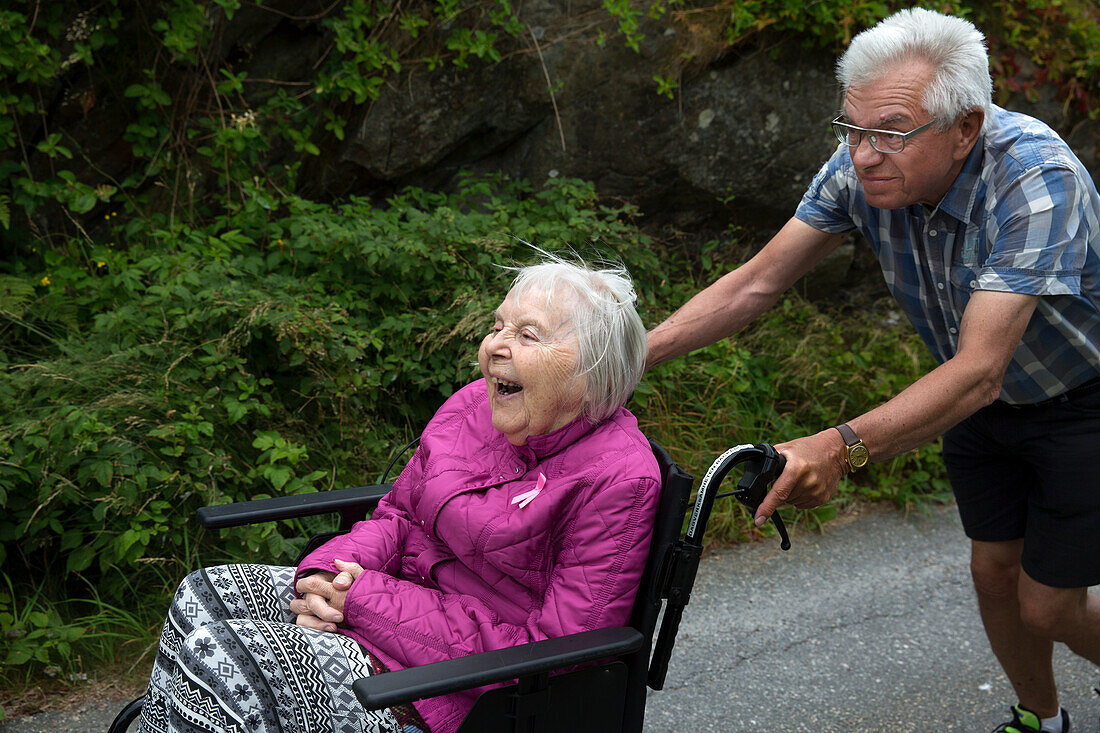 Älterer Mann schiebt ältere Frau im Rollstuhl