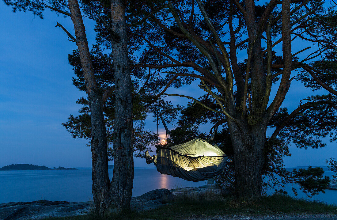 Person schlafend in Hängematte am See bei Nacht