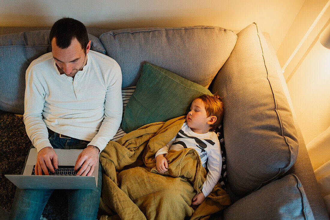 Vater benutzt Laptop im Wohnzimmer, während Tochter neben ihm schläft