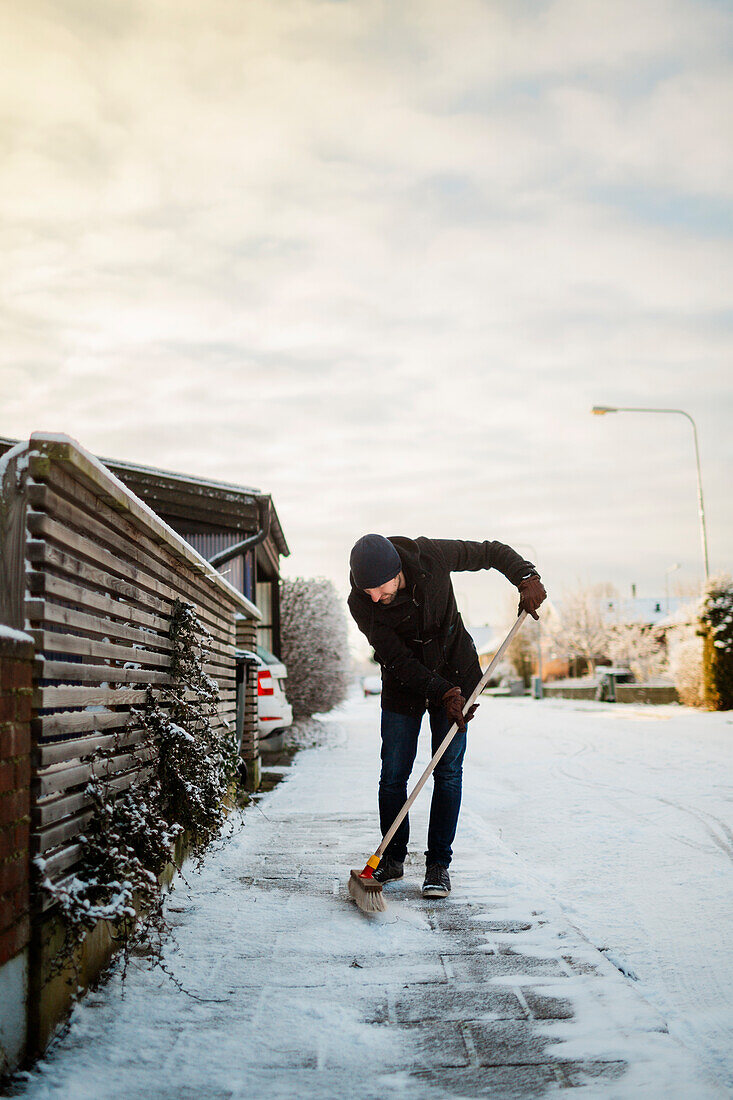 Mann entfernt mit Besen Schnee vom Gehweg