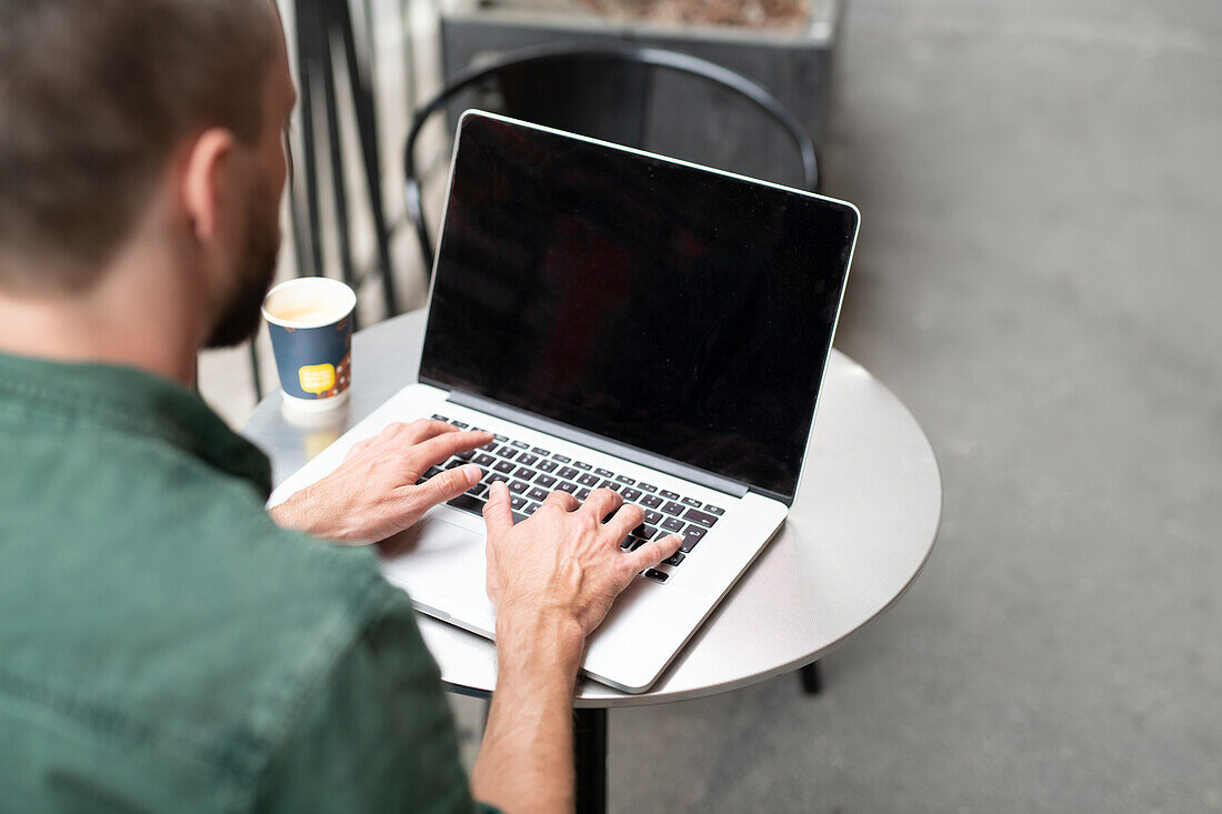 Man using laptop in outdoor cafe