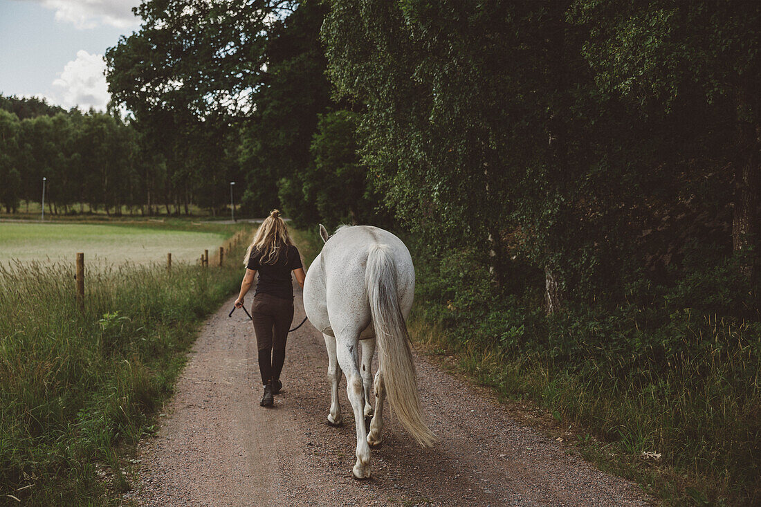 Woman walking down road with horse