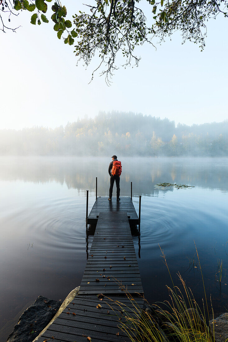 Man on pier in lake in morning fog