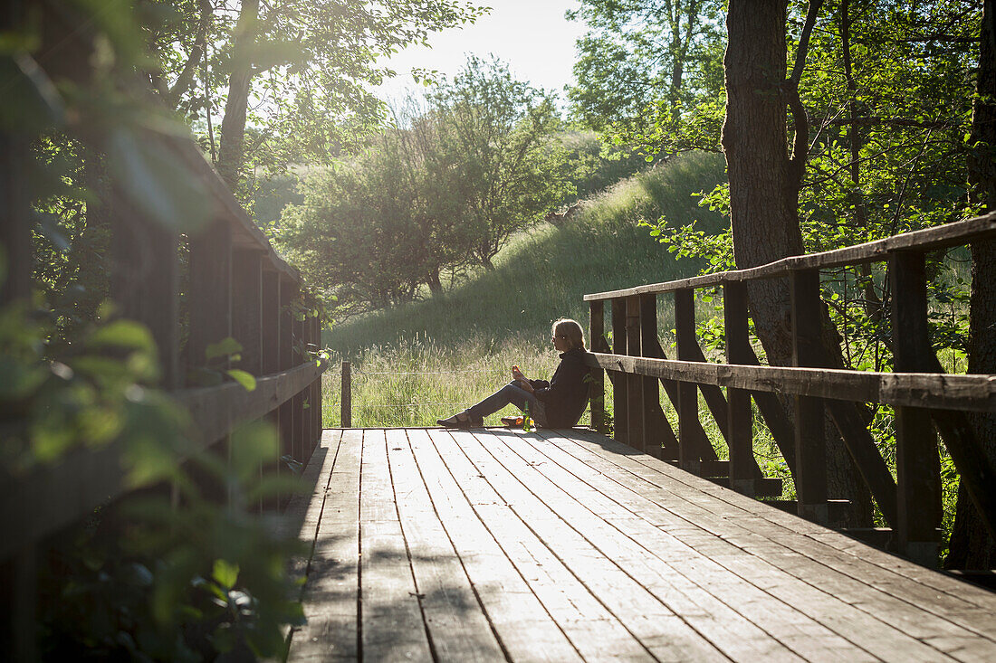 Frau sitzt auf einer Holzbrücke