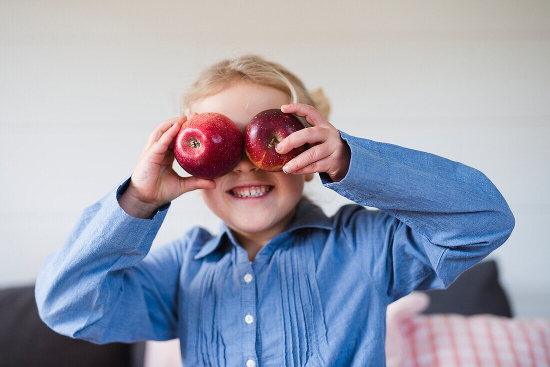 Girl holding apples over eyes