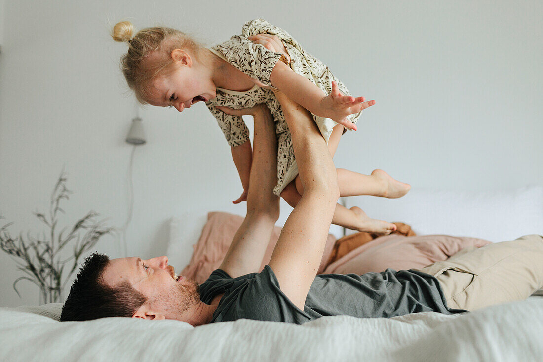 Father playing with daughter on bed