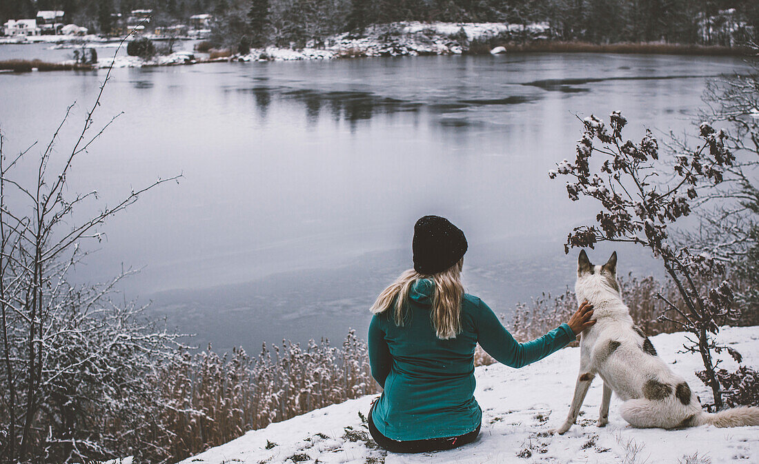 Frau mit Hund sitzend am See