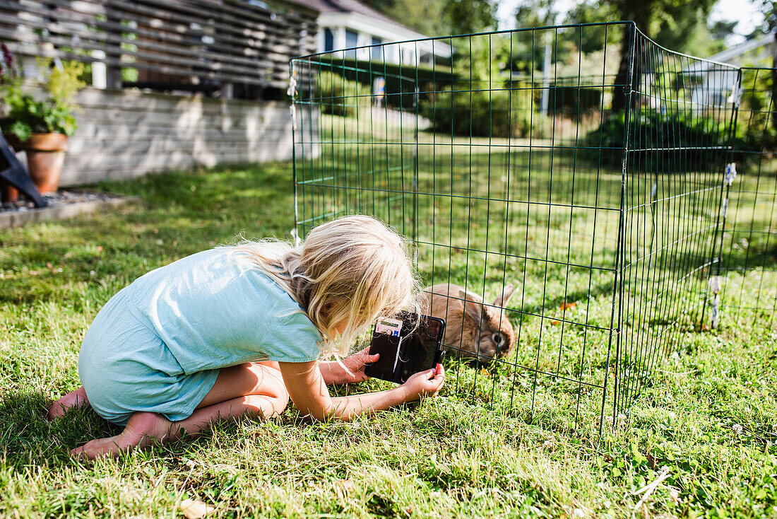 Mädchen, das ein Kaninchen im Käfig fotografiert