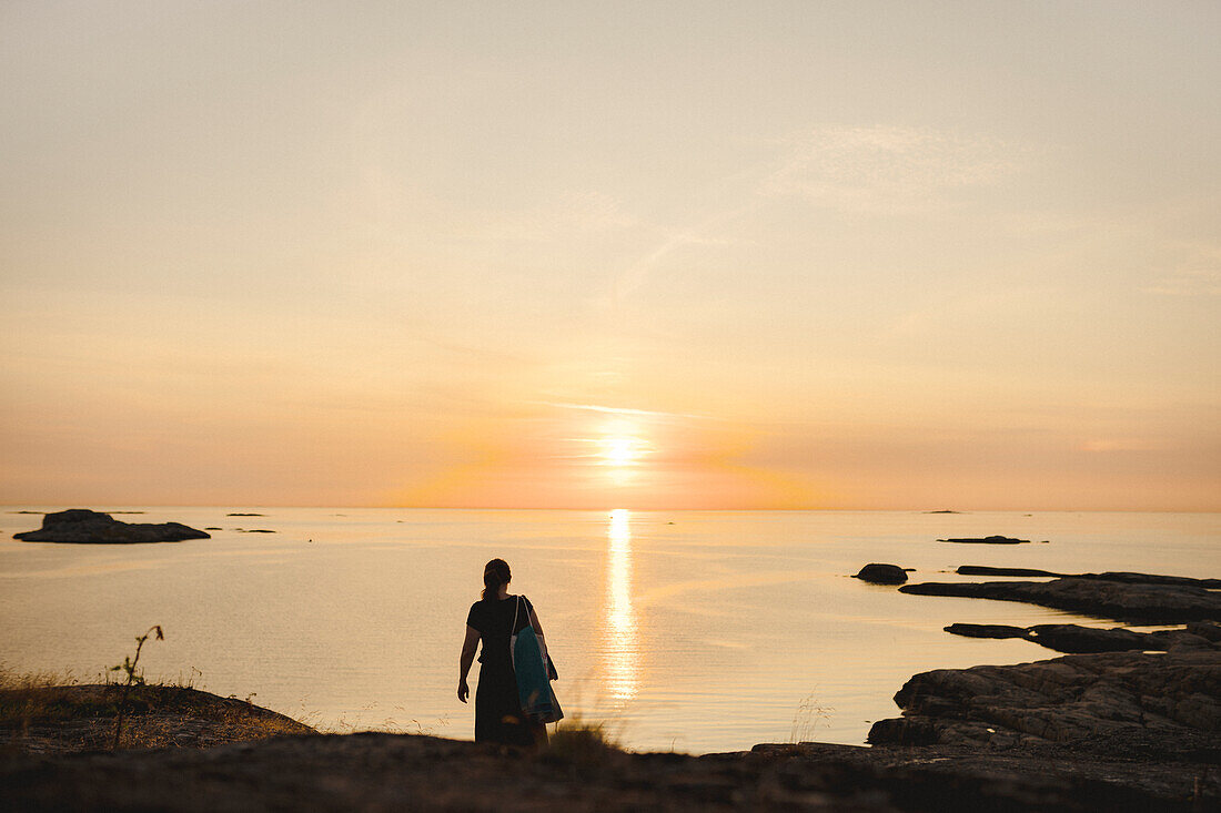 Frau an felsiger Küste bei Sonnenuntergang