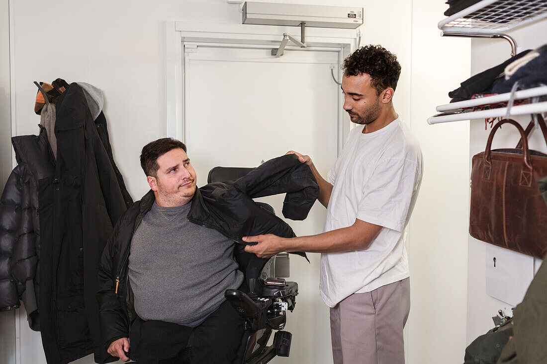 Karriere hilft Mann im Rollstuhl beim Anziehen der Jacke