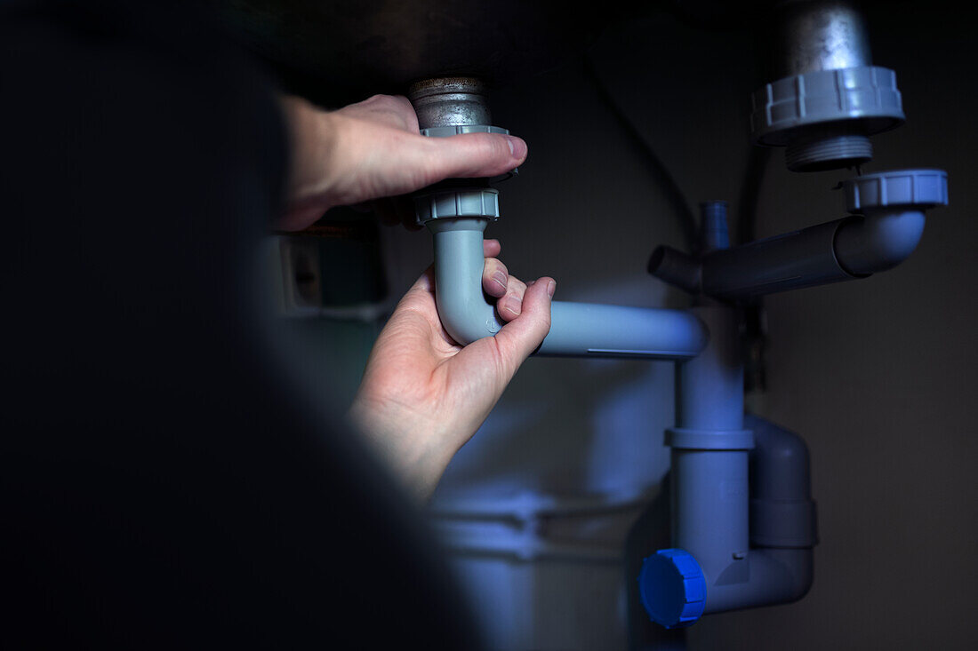 Hands of man fixing pipe under bathroom sink