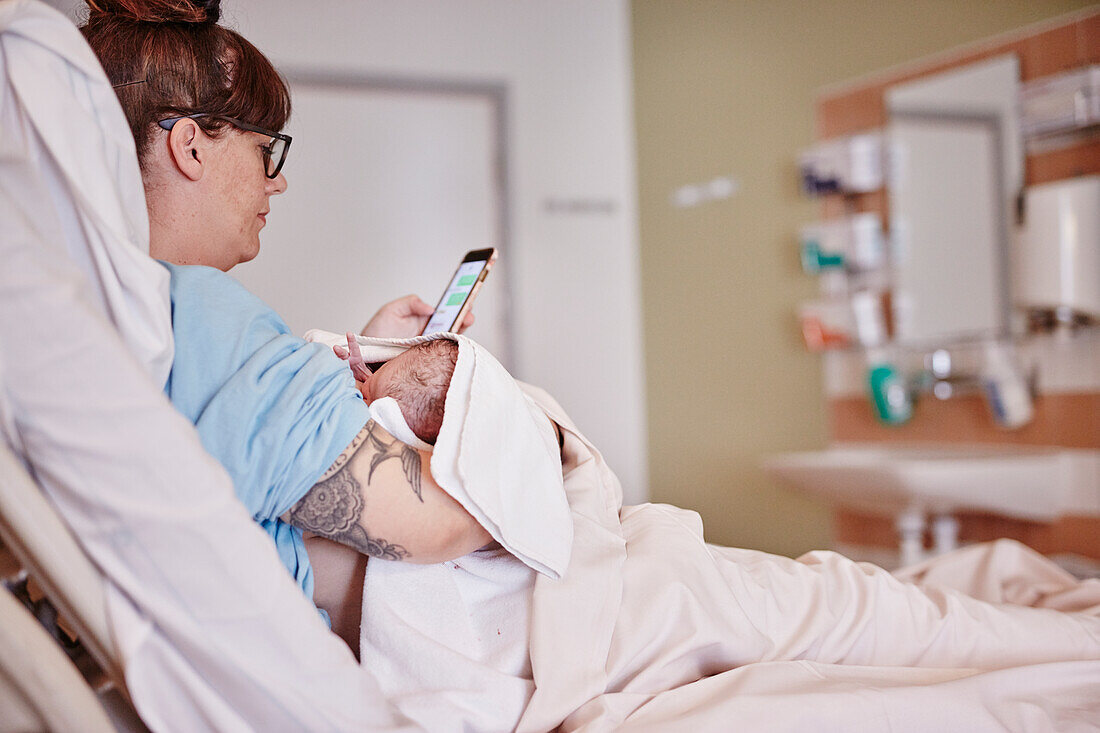 Mutter mit neugeborenem Baby im Krankenhaus beim Telefonieren