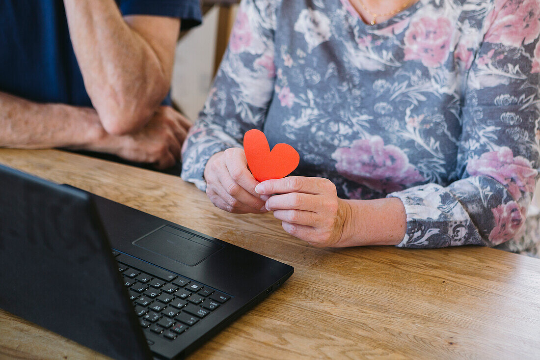 Woman holding paper heart while talking via video chat