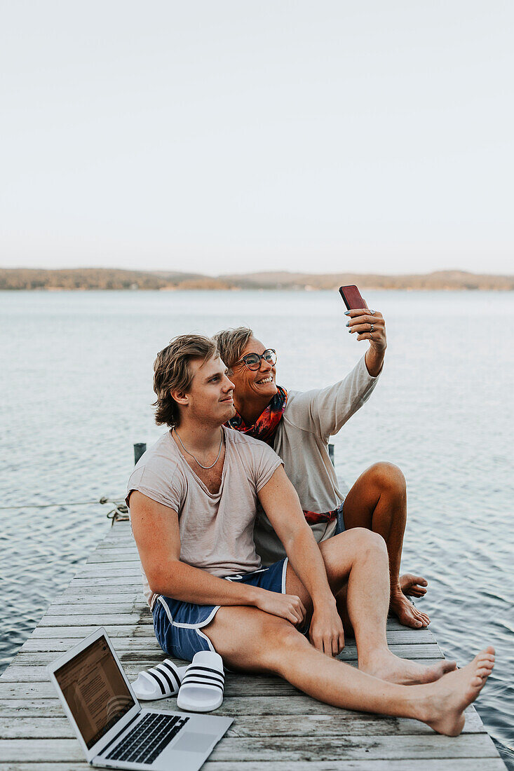 Mutter mit erwachsenem Sohn auf dem Bootssteg beim Selfie machen