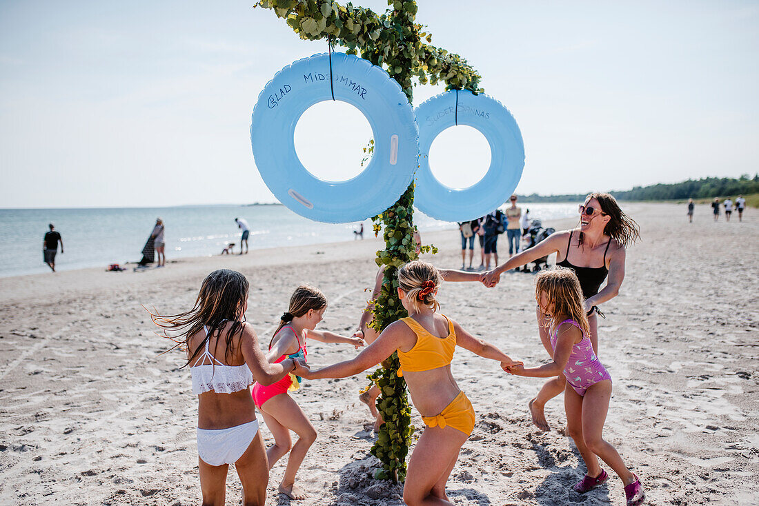 Mutter mit Töchtern, die am Strand um einen Maibaum tanzen