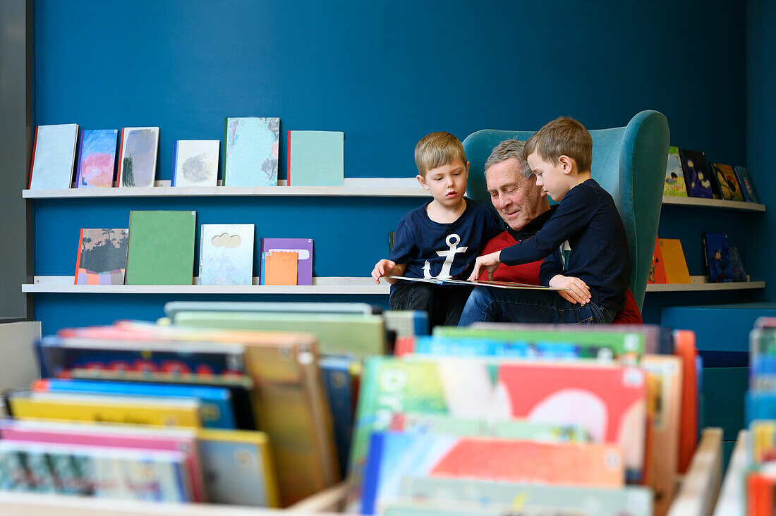 Grandfather reading book to grandsons in library