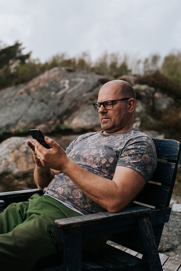 Mann auf einem Holzstuhl, der ein Mobiltelefon benutzt