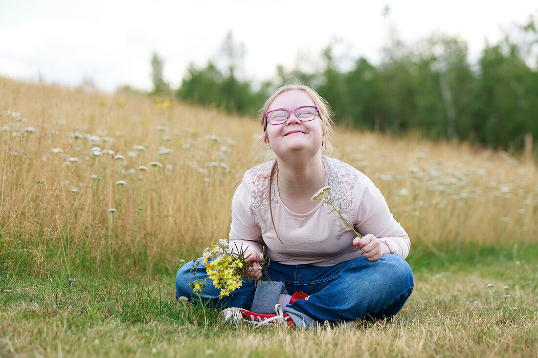 Smiling girl on meadow holding wildflowers