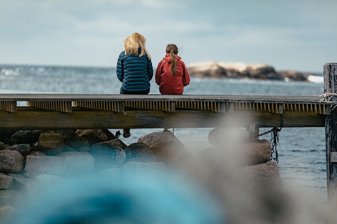 Mother and daughter sitting on jetty
