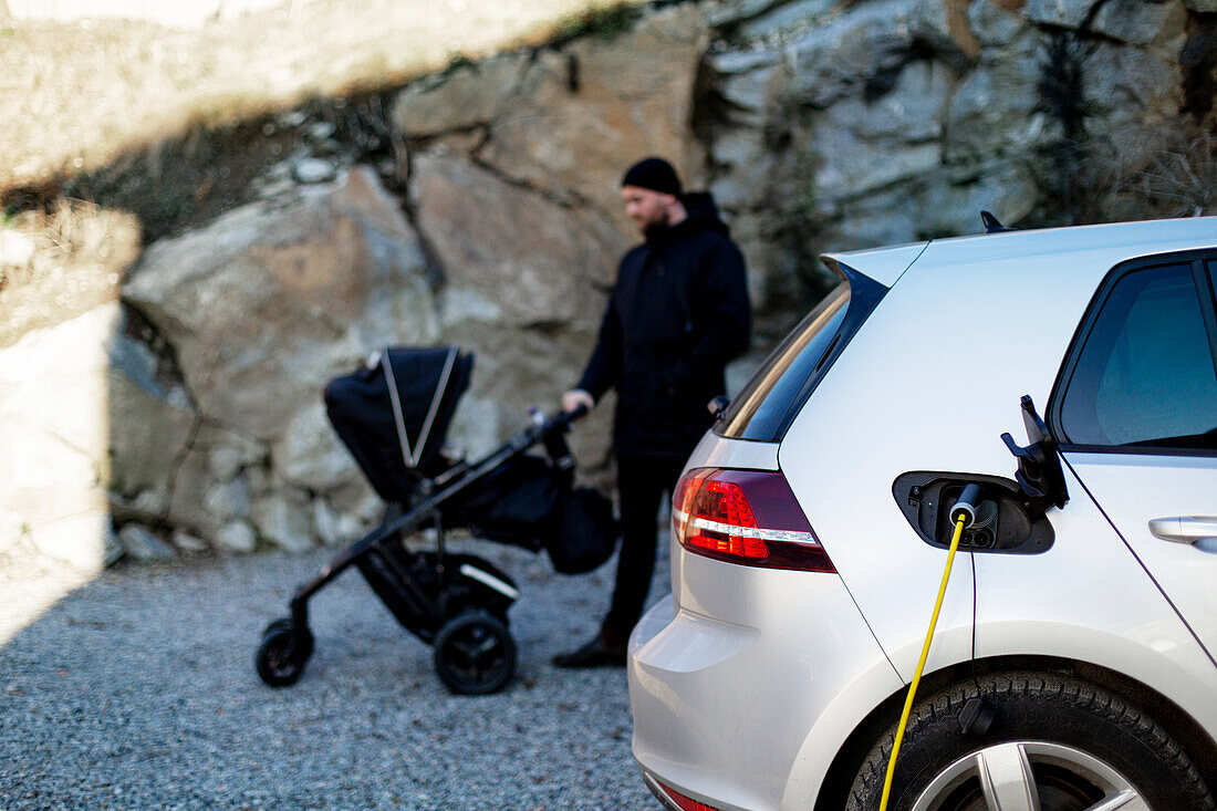 Electric car on charge, man with pram on background