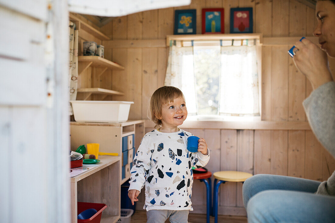 Toddler girl in playhouse playing tea party with mother