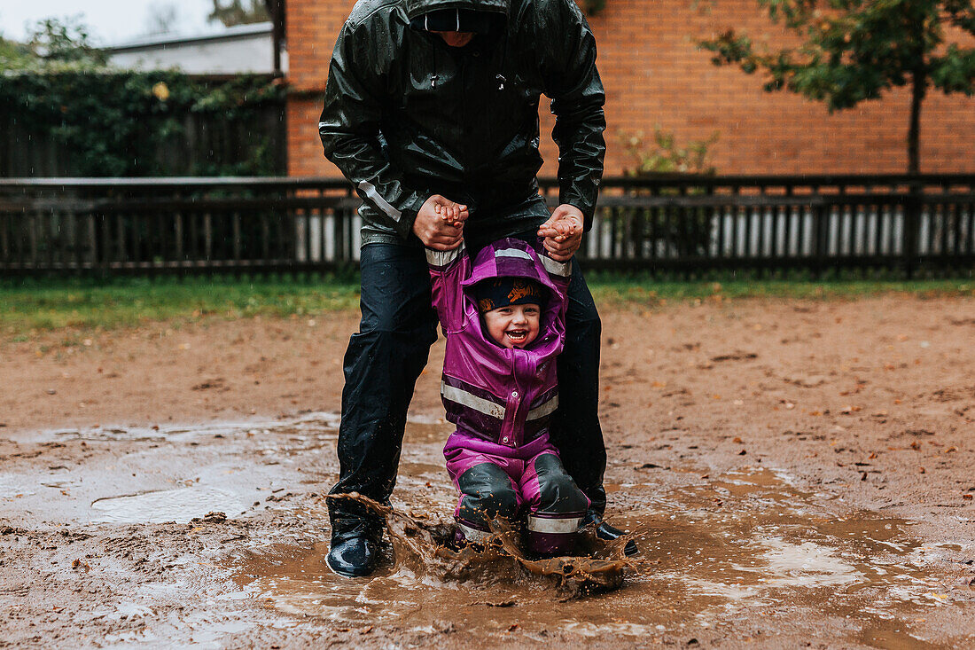 Father playing with toddler girl in puddle