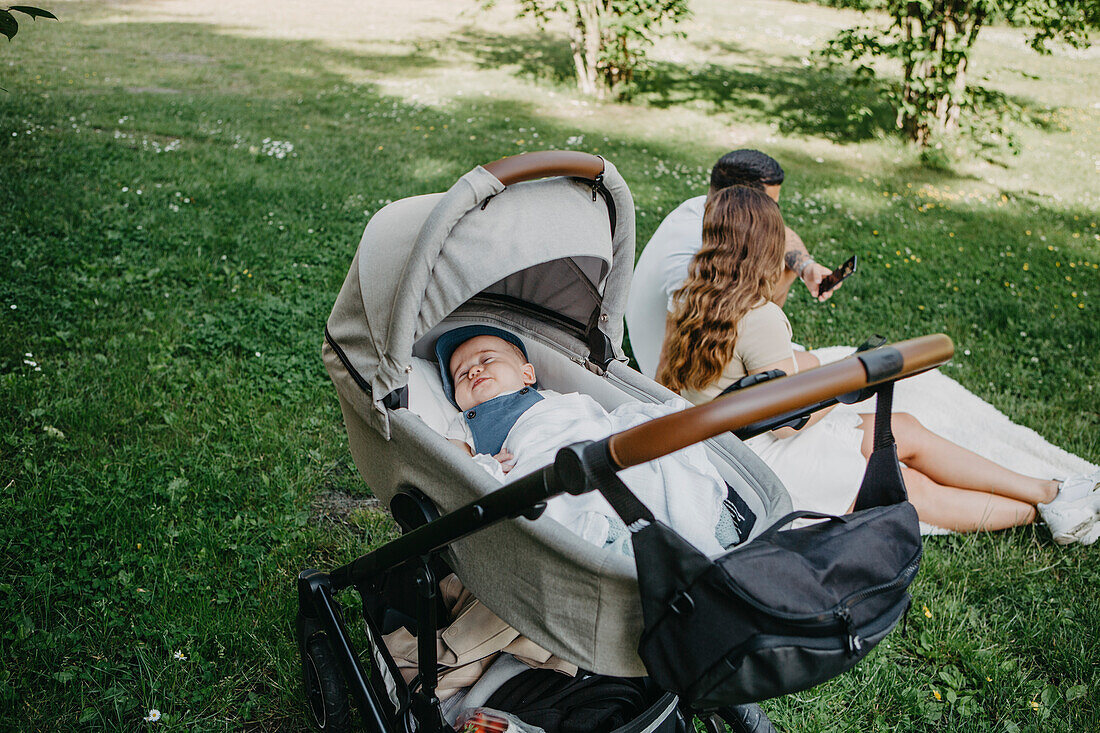 Baby boy sleeping in pram, parents in background