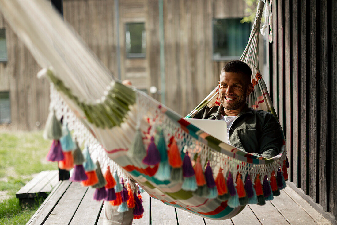 Smiling man using laptop while relaxing on hammock