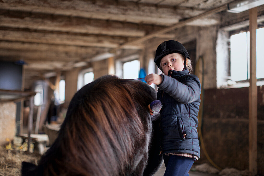 Mädchen bürstet Pferd im Stall
