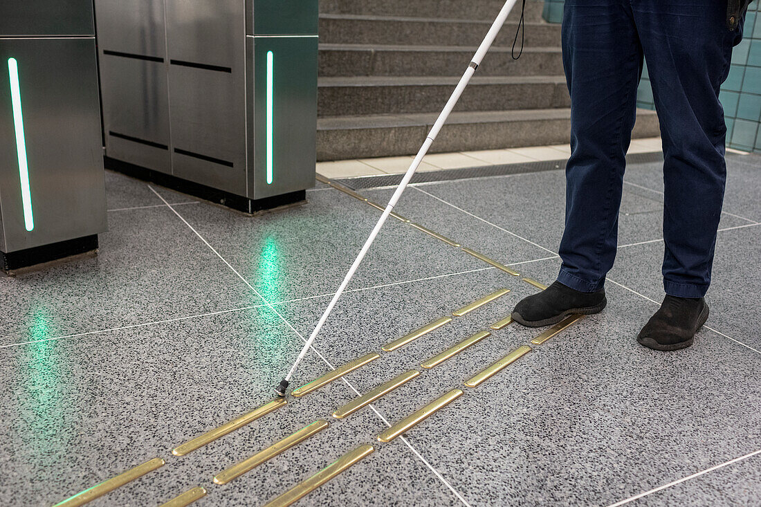 Low section of person with white cane standing at metro station