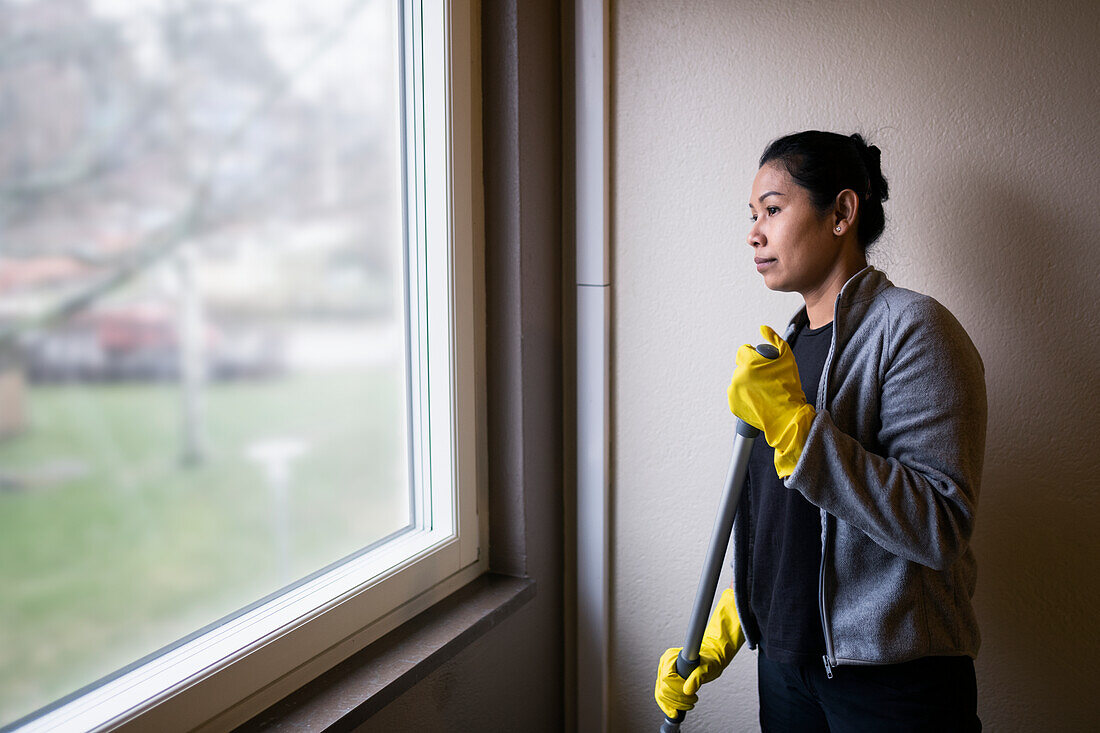 Woman holding mop and looking through window