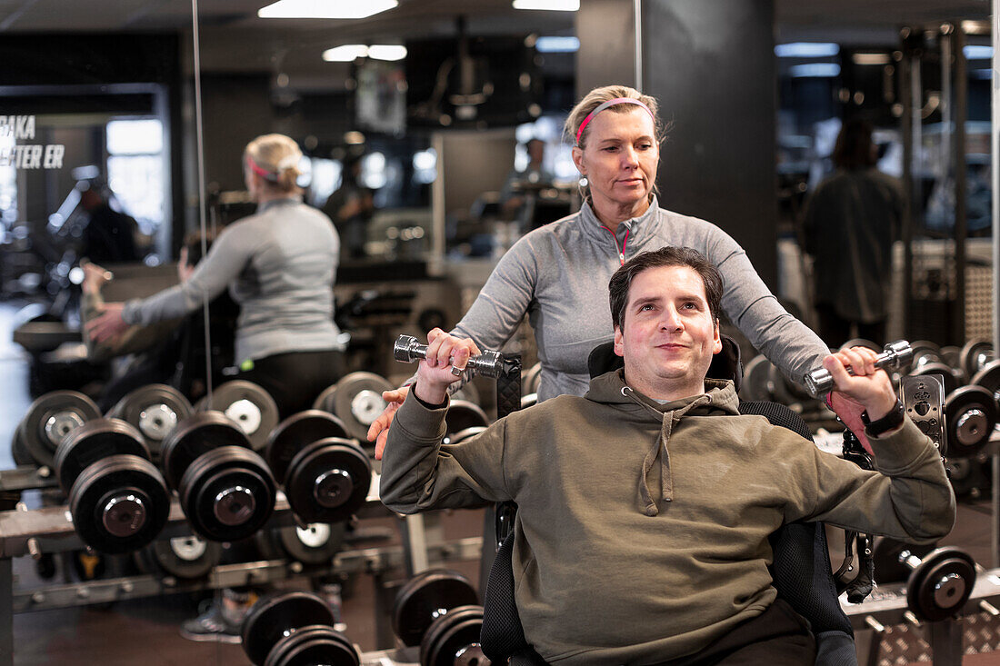 Mann im Rollstuhl trainiert im Fitnessstudio mit Personal Trainer