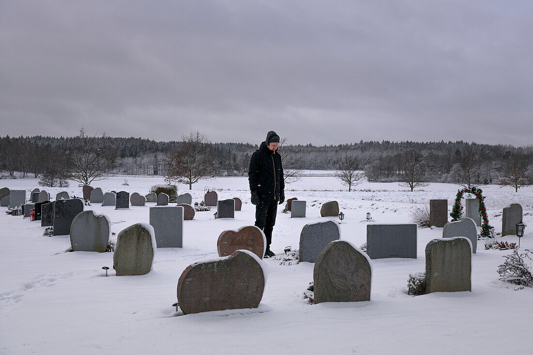 Mann steht über einem Grab auf dem Friedhof