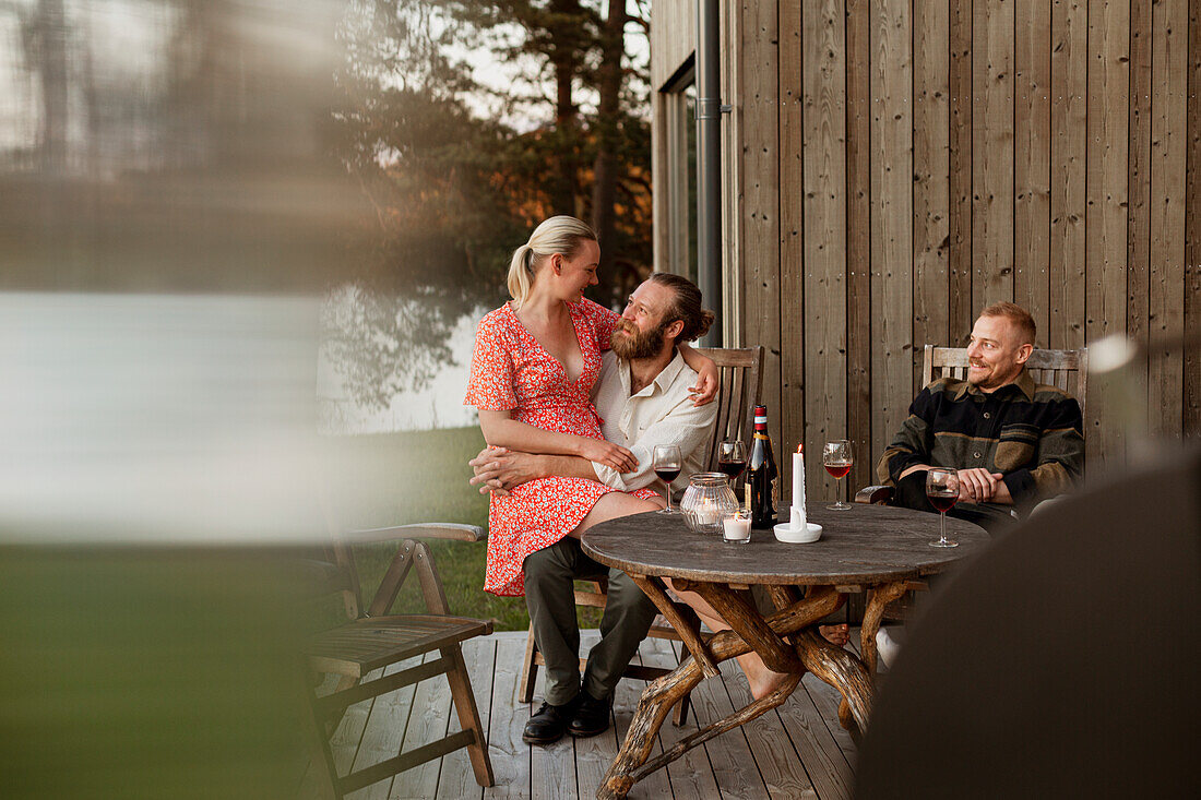 Pärchen mit Freund sitzt auf Terrasse und trinkt Wein