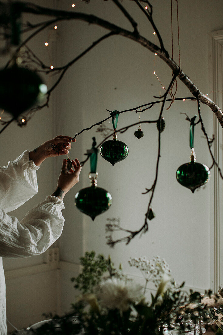 Woman hanging Christmas ornaments on branch