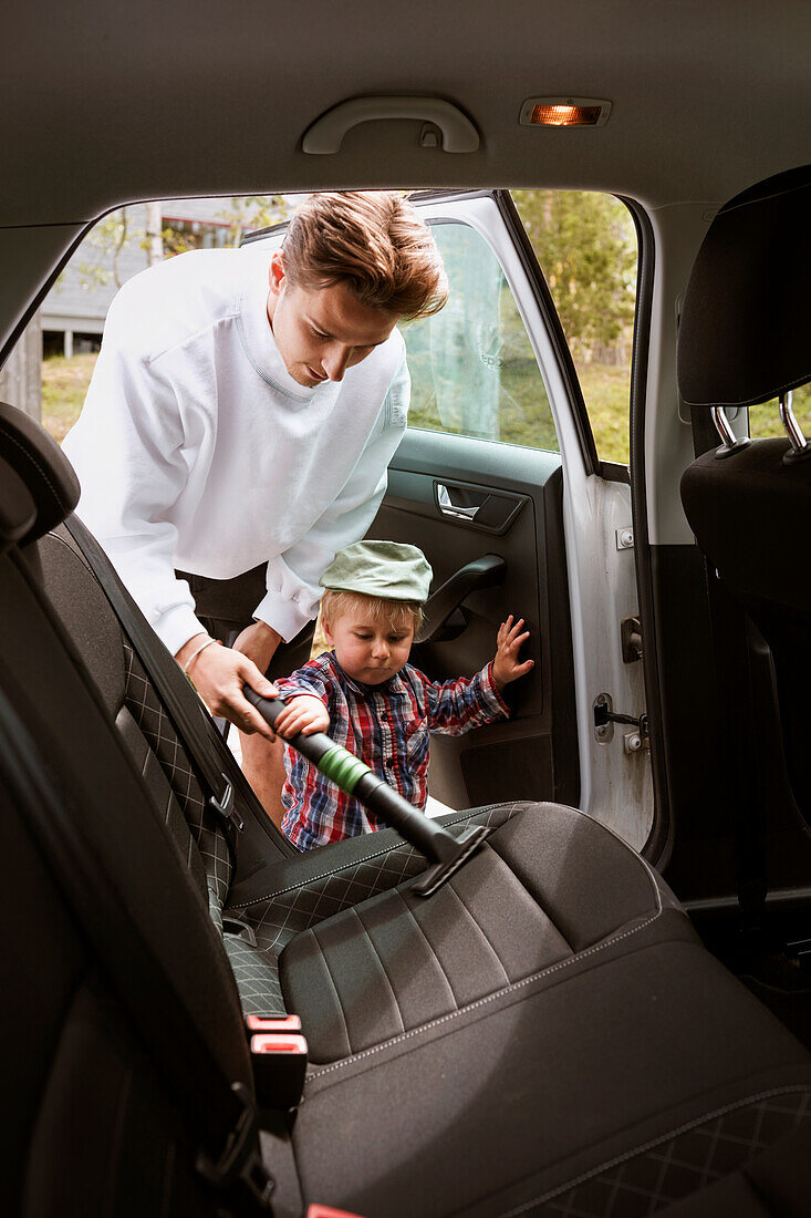 Mann mit Kleinkind beim Staubsaugen im Auto