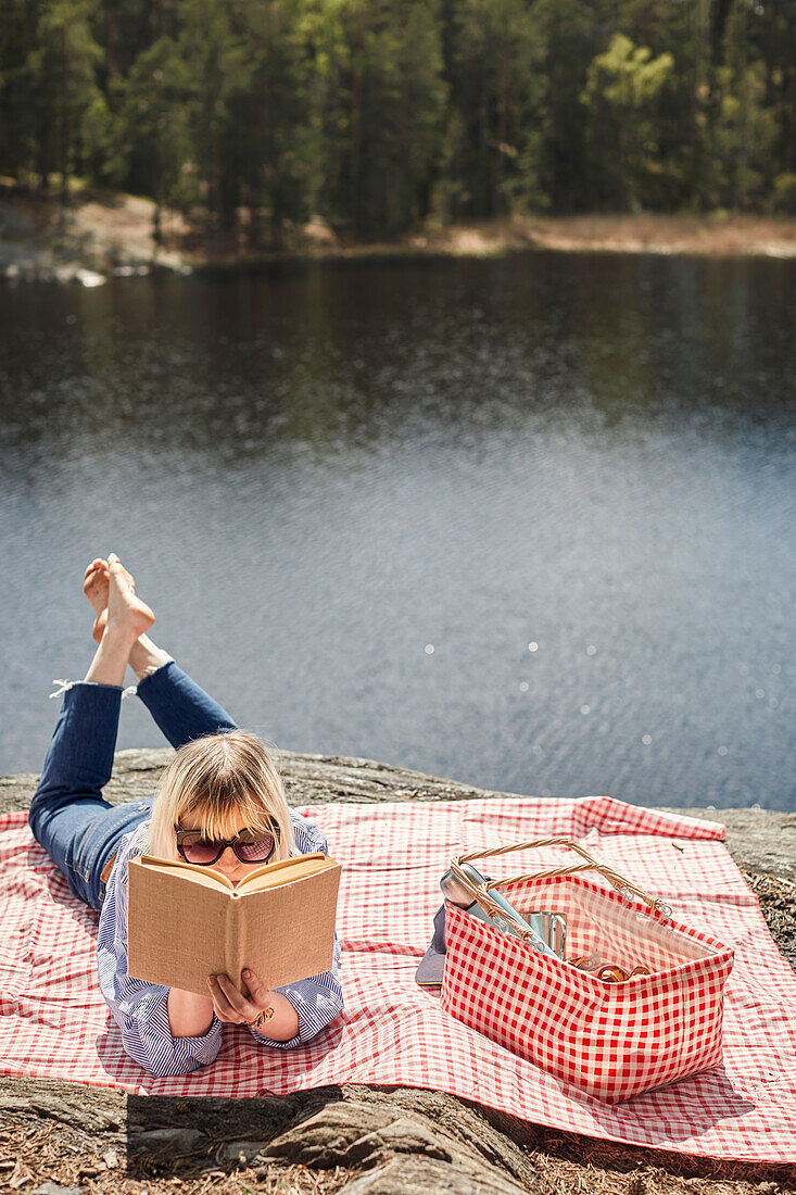 Frau liegt auf einer Picknickdecke und liest ein Buch