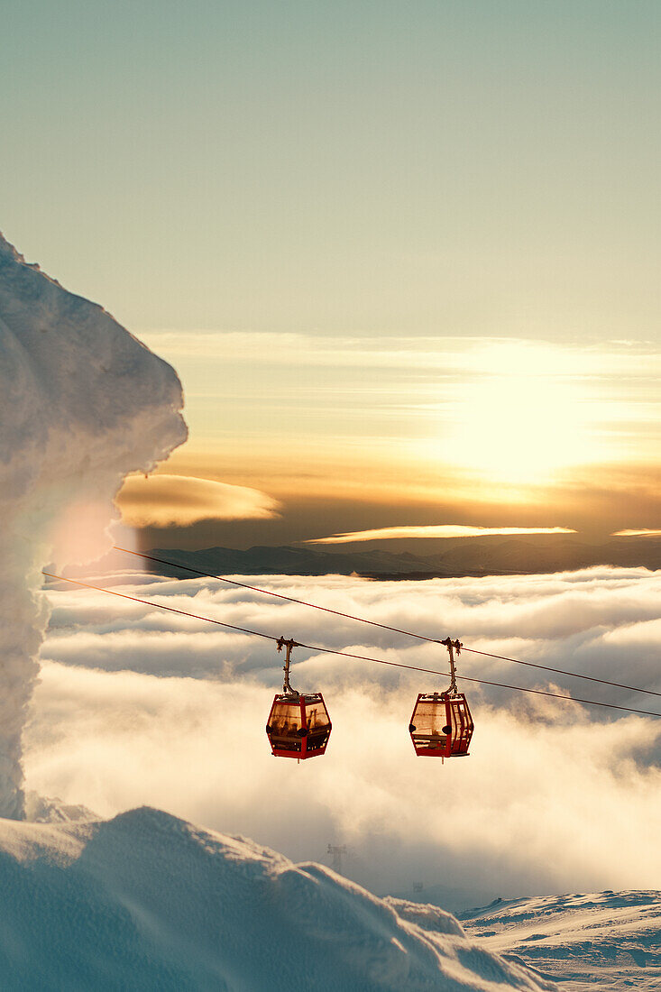 Ski lifts above clouds at sunset