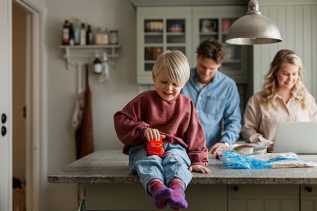 Junge spielt in der Küche, Eltern im Hintergrund