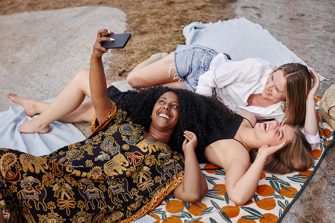 Three friends lying on blanket and taking selfie