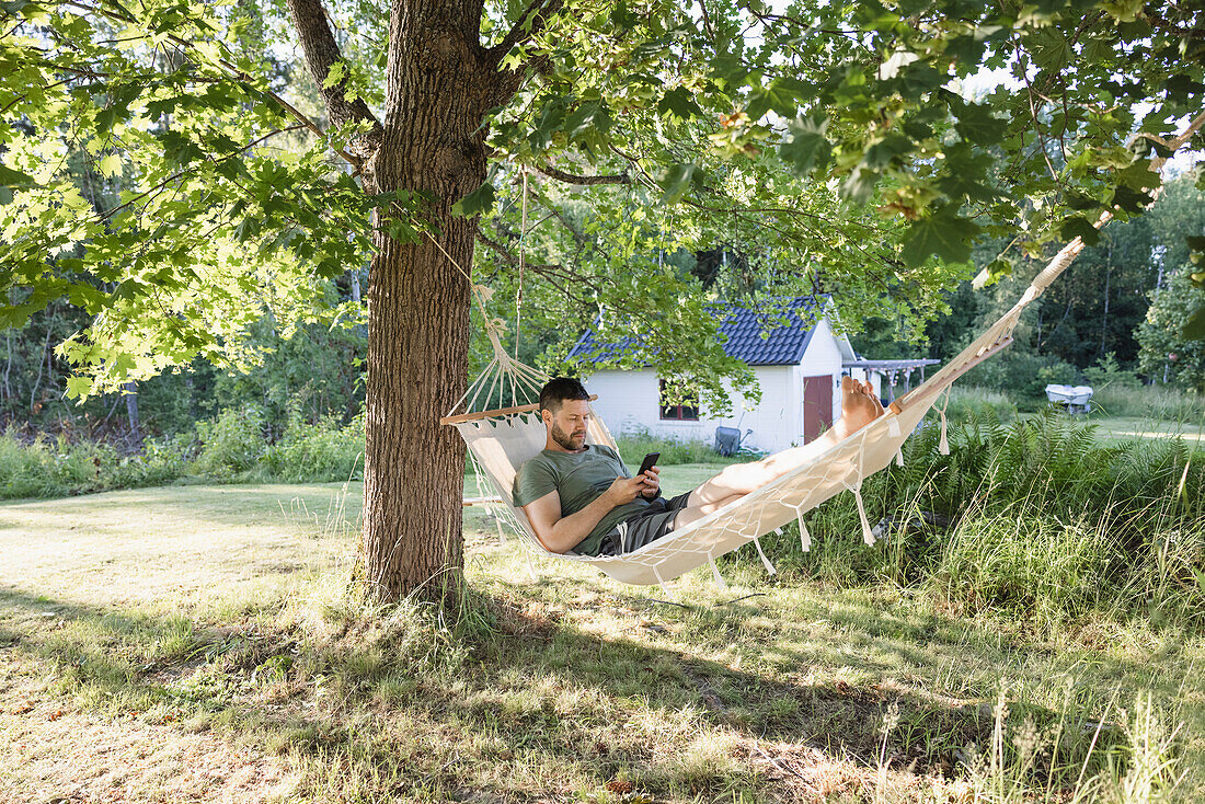 Man lying in hammock in garden and using phone