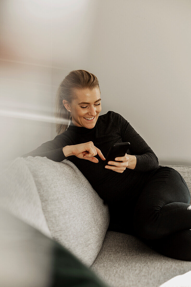 Smiling woman on sofa using cell phone