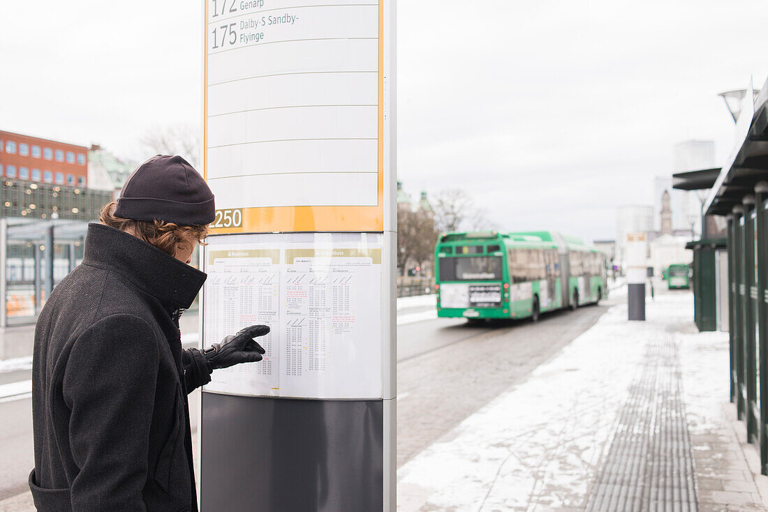 Junger Mann prüft Fahrplan an der Bushaltestelle