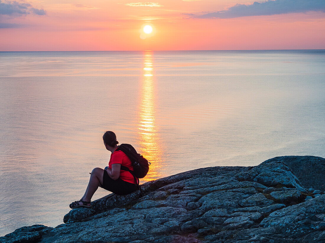 Frau sitzt auf einem Felsen und betrachtet den Sonnenuntergang über dem Meer