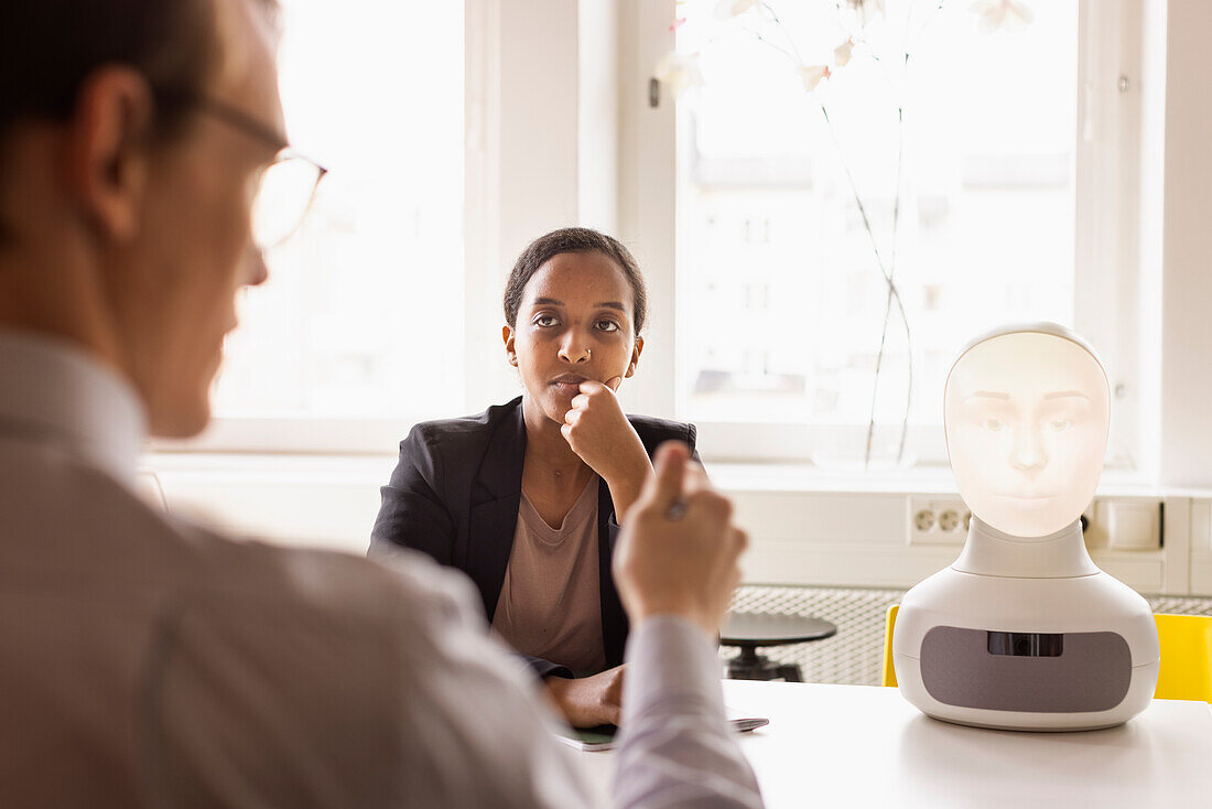 Business people discussing robot voice assistant during meeting