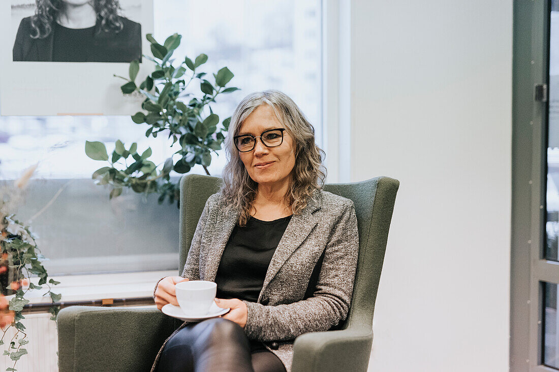 Frau sitzt im Stuhl mit Kaffeetasse