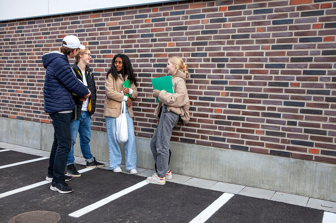 Group of students standing against brick wall and talking