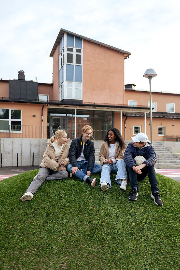 Teenage friends sitting on lawn in front of school