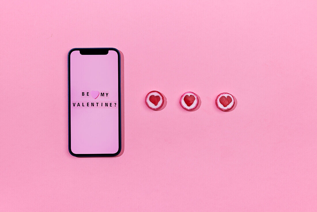 Smartphone and heart-shaped candies on pink background