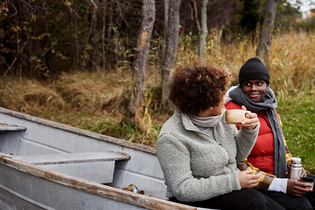 Friends sitting in old boat and drinking hot drinks